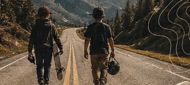 Two kids walking down a mountain road with a skateboard and helmet